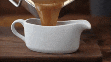 gravy is being poured into a gravy boat on a wooden cutting board .