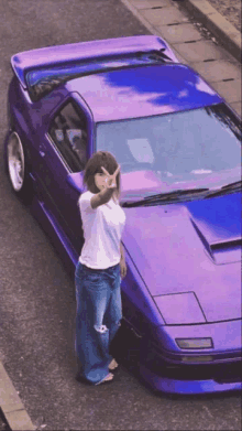 a woman stands in front of a purple car giving a peace sign