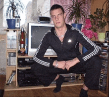 a man squatting in front of a television with a clock on the wall that says 12:02