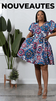 a woman wearing a blue and purple floral dress is standing in front of a plant