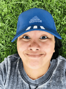 a woman wearing a blue adidas hat laying on the grass