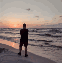 a man stands on a beach looking at the sunset