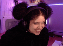 a woman with curly hair wearing headphones smiles in front of a purple wall