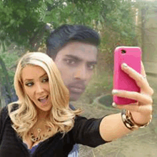 a woman is taking a selfie with a pink phone while a man is behind her .