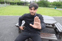 a man sitting at a picnic table with his hand up