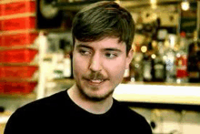 a man with a mustache is wearing a black shirt and standing in front of a bar .