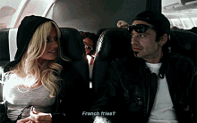 a man and a woman are sitting on a plane and the man is asking the woman if she wants french fries