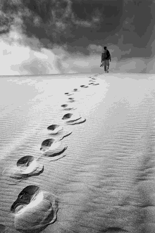 a black and white photo of a person walking on a sandy hill