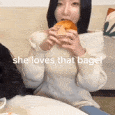 a woman in a white sweater is eating a bagel