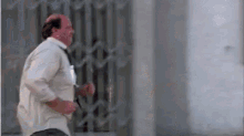 a bald man in a white shirt and tie is running across a street .