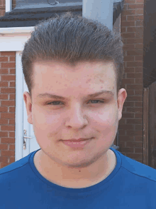 a young man wearing a blue shirt stands in front of a brick wall