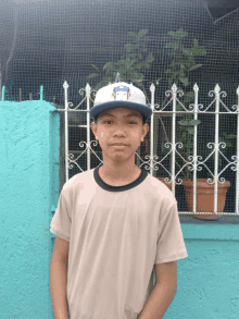 a young boy wearing a hat with the word la on it stands in front of a fence