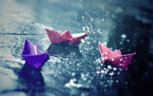 three paper boats are floating in the rain