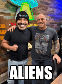 two men are posing for a picture with the word aliens in the corner