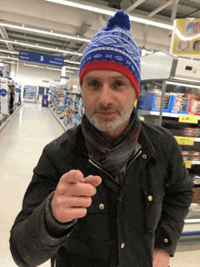 a man wearing a blue and red hat points at the camera in a store