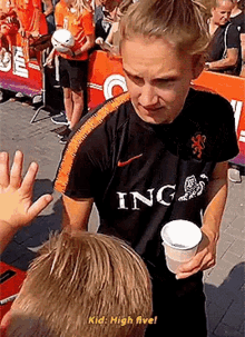 a female soccer player is giving a high five to a young boy while holding a cup of coffee .