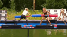 two women are playing a game of tug of war over a body of water with a sign in the background that says ' you '