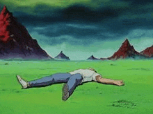 a man is laying on his stomach in a field with mountains in the background .