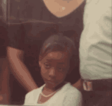 a little girl wearing a pearl necklace is sitting in a family photo