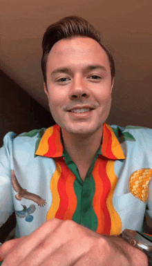 a man wearing a colorful shirt with birds on it is smiling