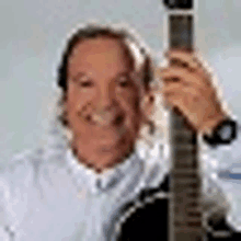 a man is holding a guitar in his right hand and smiling .