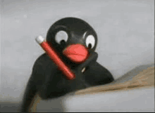 a black penguin with a red beak is holding a red pencil .