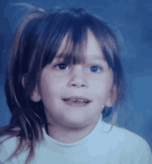 a little girl with a ponytail and a white shirt smiles for the camera