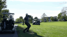 a man swings a golf club on a golf course next to a golf cart