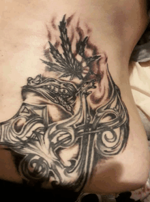 a black and white tattoo on a person 's stomach with a leaf and a cross