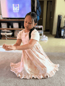 a little girl in a pink dress is kneeling on the floor in front of a tv that says disney