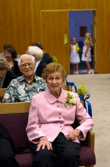 a woman in a pink jacket sits next to a man in a floral shirt in a church