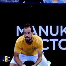 a man in a yellow shirt is holding a tennis racquet in front of a sign that says manuk tc