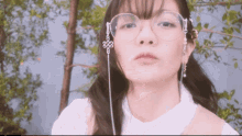 a woman wearing glasses and earrings looks at the camera with trees in the background