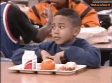 a young boy is sitting at a table with a tray of food and a milk carton on it .