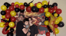 a man holds a child in front of a wall with balloons and the word day on it