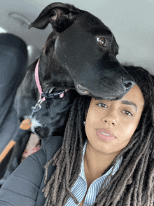 a woman with dreadlocks sits in a car with a black dog