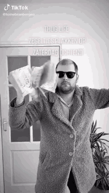 a man wearing sunglasses and a coat is holding a roll of toilet paper