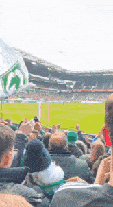 a crowd of people watching a soccer game in a stadium with a green and white flag with the letter o on it