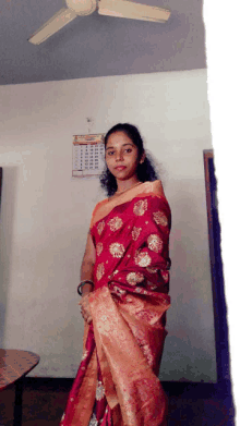 a woman in a red and gold saree stands in front of a wall calendar that shows the month of october