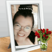 a framed picture of a woman with glasses next to a vase of flowers