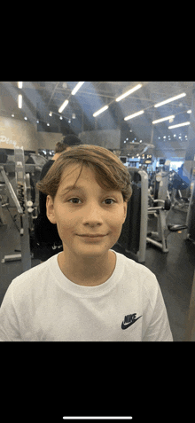 a young boy wearing a white nike t-shirt is standing in a gym