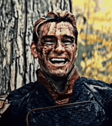 a man with blood on his face is laughing while standing in front of a tree .