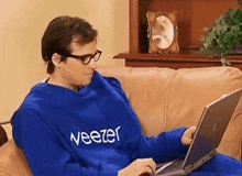 a man wearing a blue sweater that says veezer is using a laptop