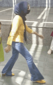 a woman in a yellow shirt and blue jeans is walking on a tiled floor