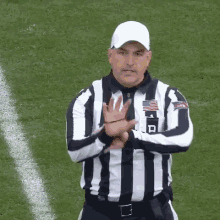 a referee wearing a black and white striped shirt and a white hat is standing on a field with his arms crossed .