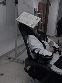 a girl is sitting in a chair with a piece of paper on her head .