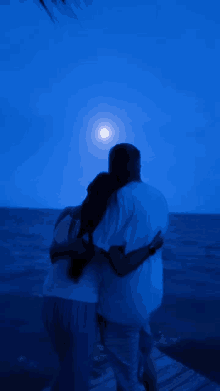 a man and a woman are hugging while looking at the full moon