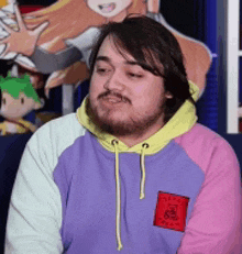 a man with a beard is wearing a purple , pink , and yellow sweatshirt .