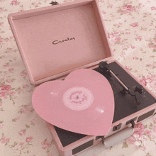 a pink crosley record player with a heart shaped record on top of it