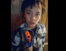 a young boy in a plaid shirt is holding a toy gun in his hand .